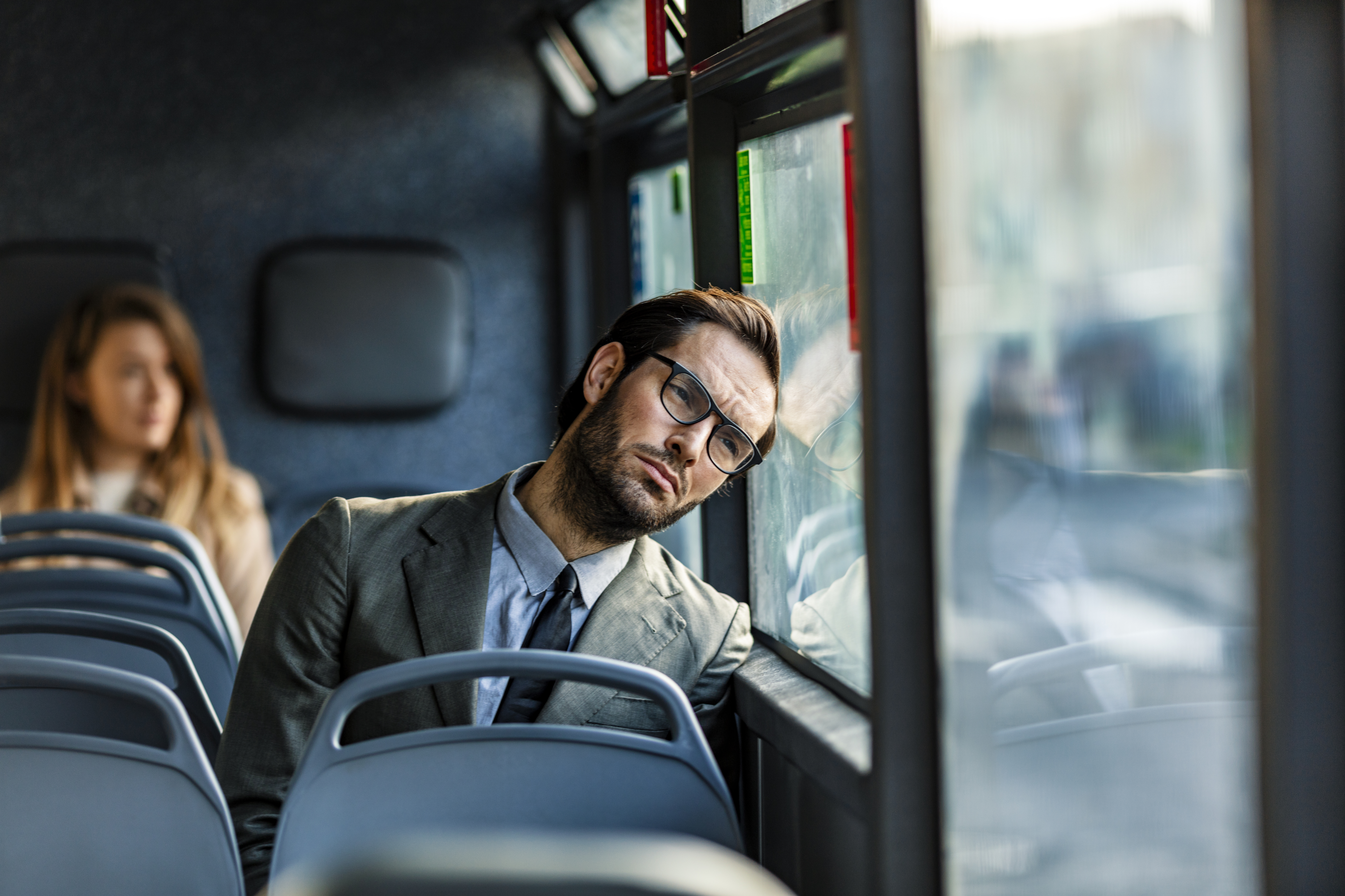 Tired businessman leaning head on bus window