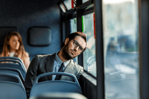 Tired young businessman sitting on the bus and day dreaming while leaning on the window during the day.