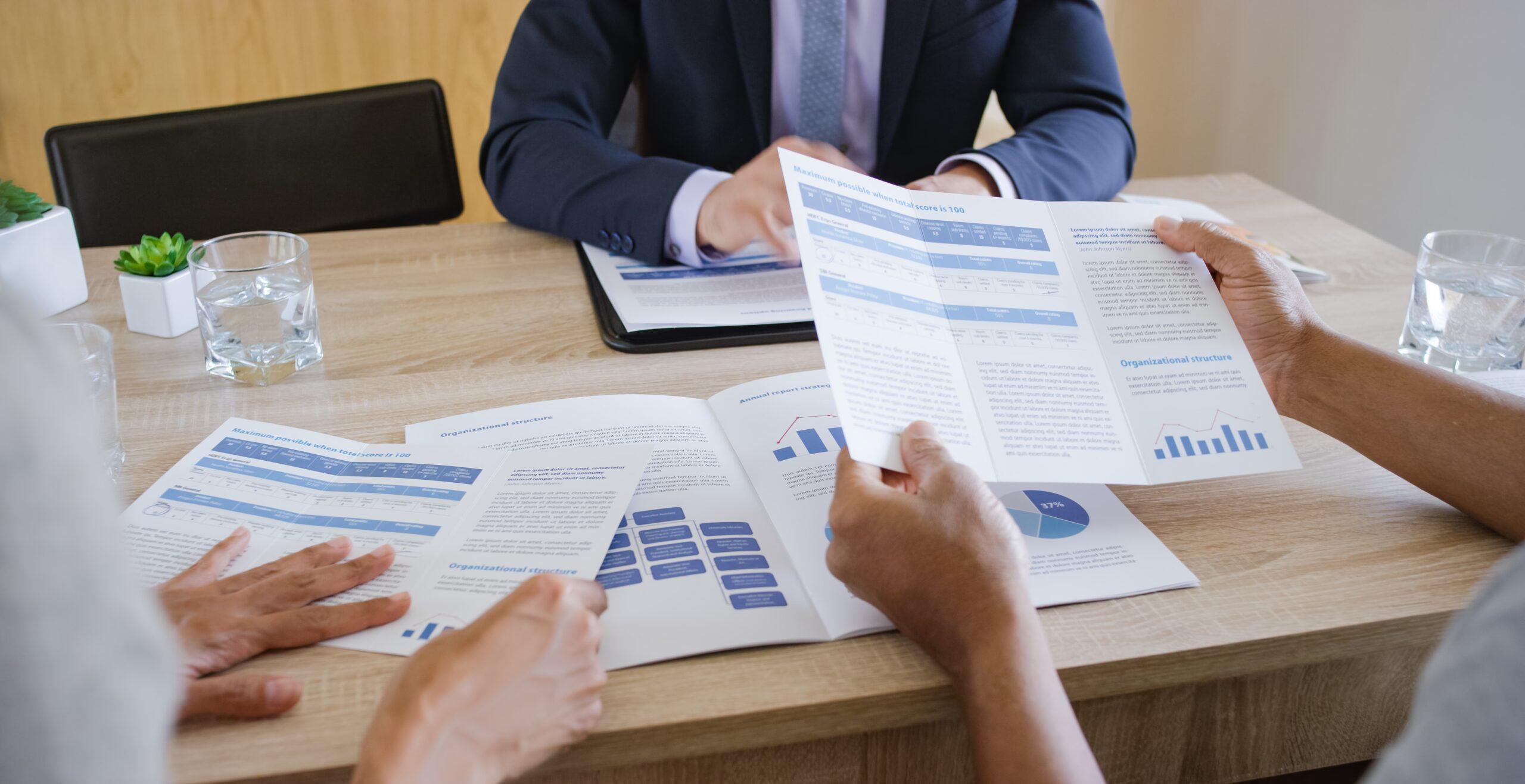 Two people look at brochures while a third person sits across the table.