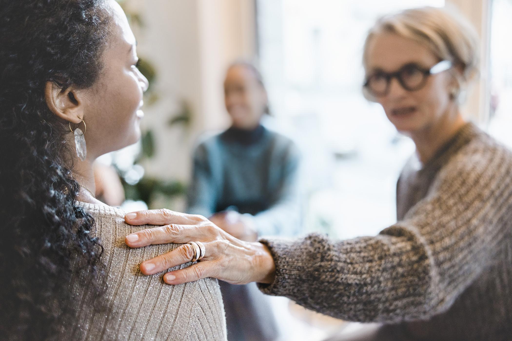 Therapist reaches out to touch the shoulder of a behavioral health client in a support group.