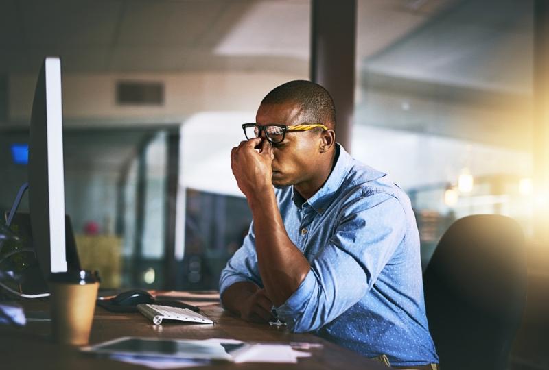 Black male in office looks stressed at desk.