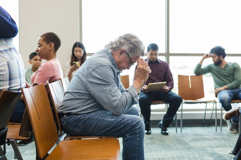 Senior adult man sits in the waiting room with his head in his hands